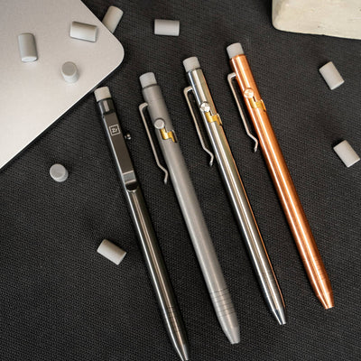 Set of four bolt action mechanical pencil pens by Big Idea Design LLC in various metallic finishes on a black surface