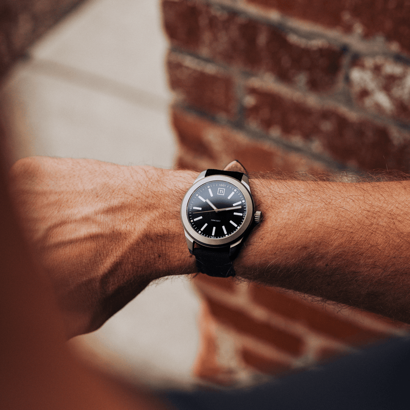 Big Idea Design LLC titanium field watch on a male wrist with black dial and leather strap