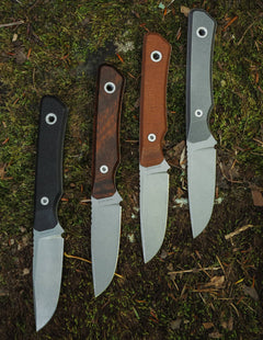 USA Machine Shop fixed knife blade collection with black, brown, and gray handles on a mossy background