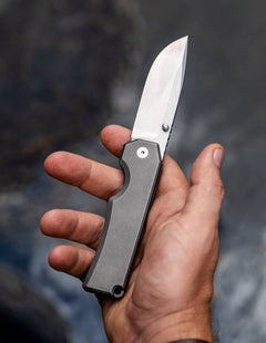 BIG IDEA DESIGN LLC titanium pocket knife with sleek blade held in hand over blurred background