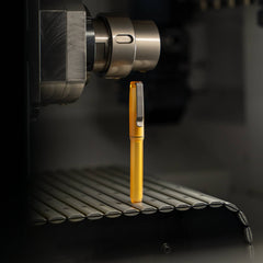 BIGiDESIGN-USA yellow USA made EDC pen standing upright on a metal surface near industrial machinery